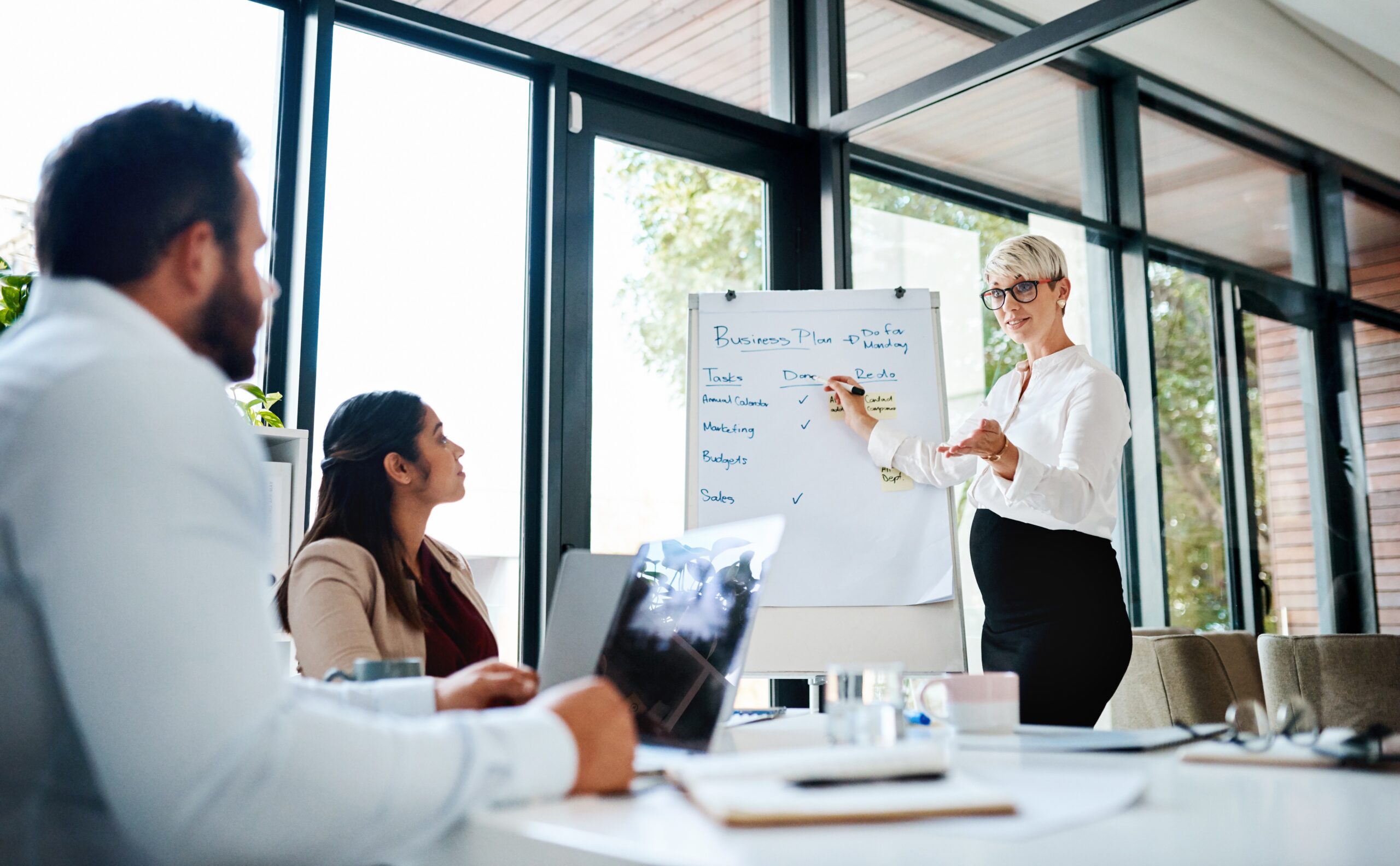 A business professional presenting a sales plan on a whiteboard during a strategy meeting.