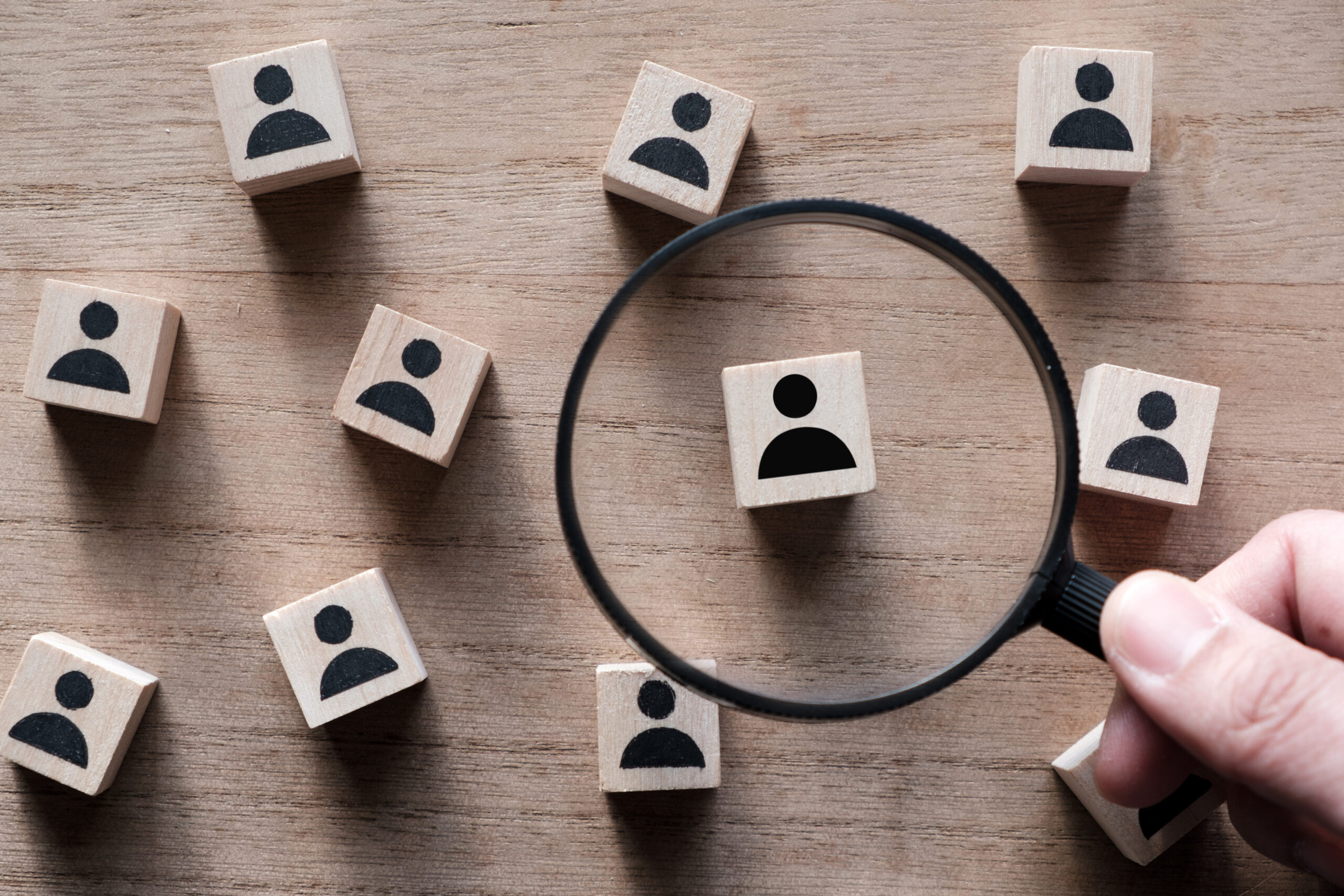 Magnifying glass highlighting a single profile among many icons, symbolizing targeted prospecting techniques to identify the right opportunities.